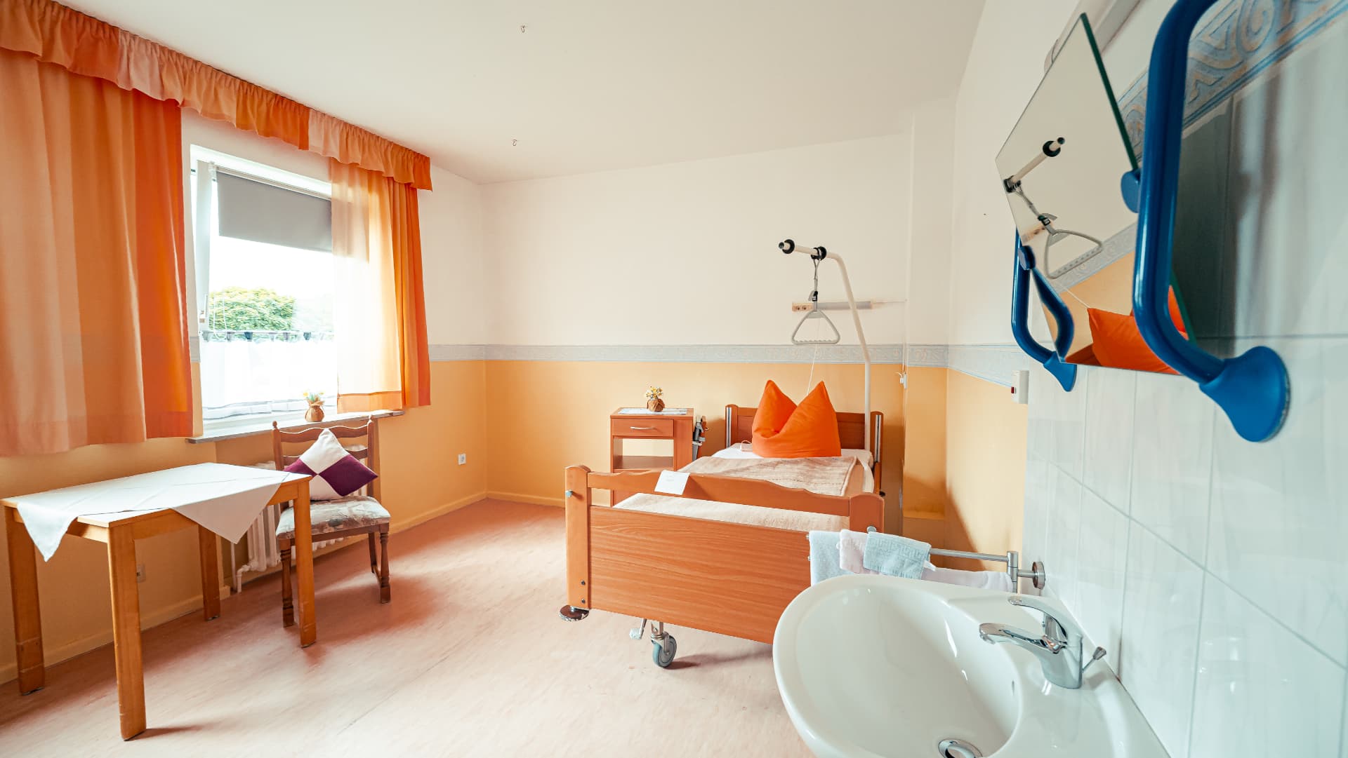 Helles Einzelzimmer mit Pflegebett, Tisch und Fenster